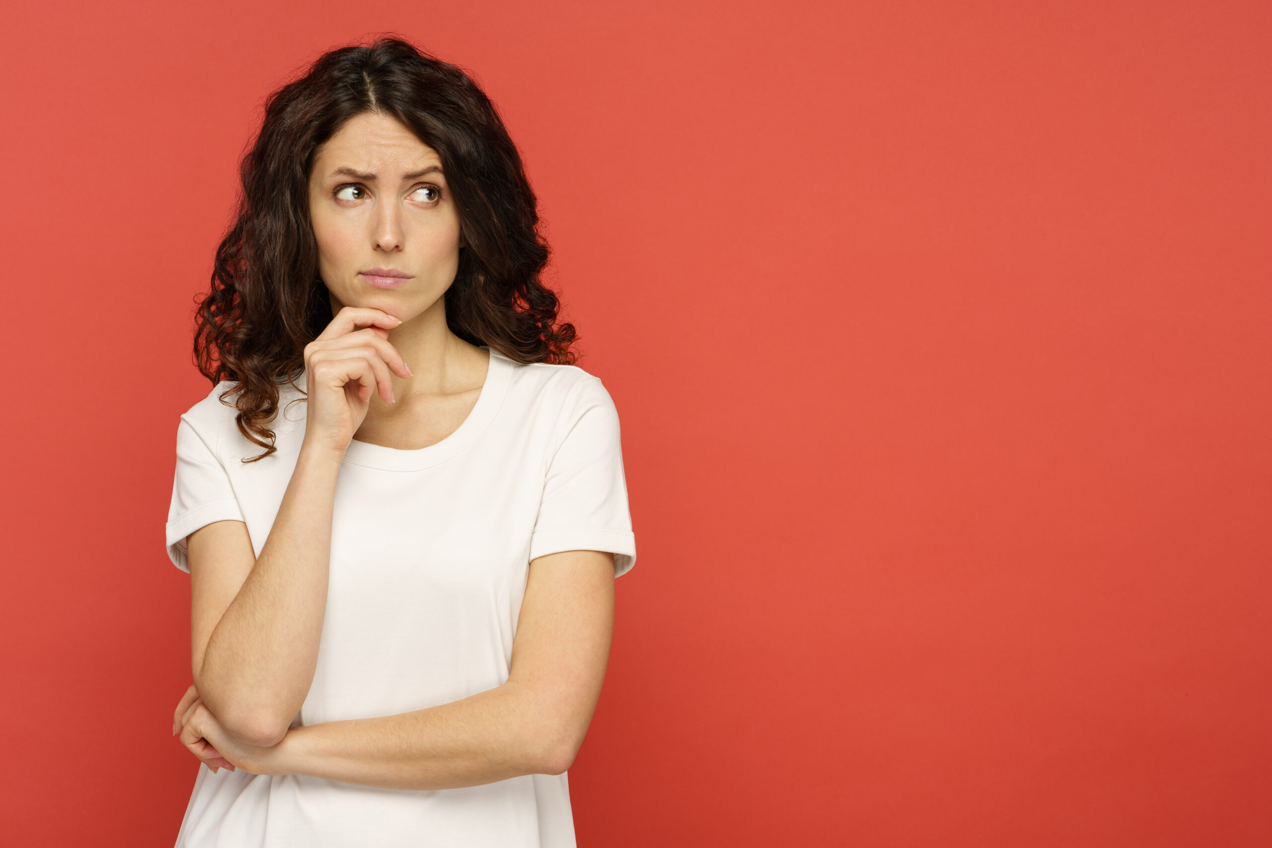 Portrait of doubtful young female pensive think with folded arms look up over red studio background