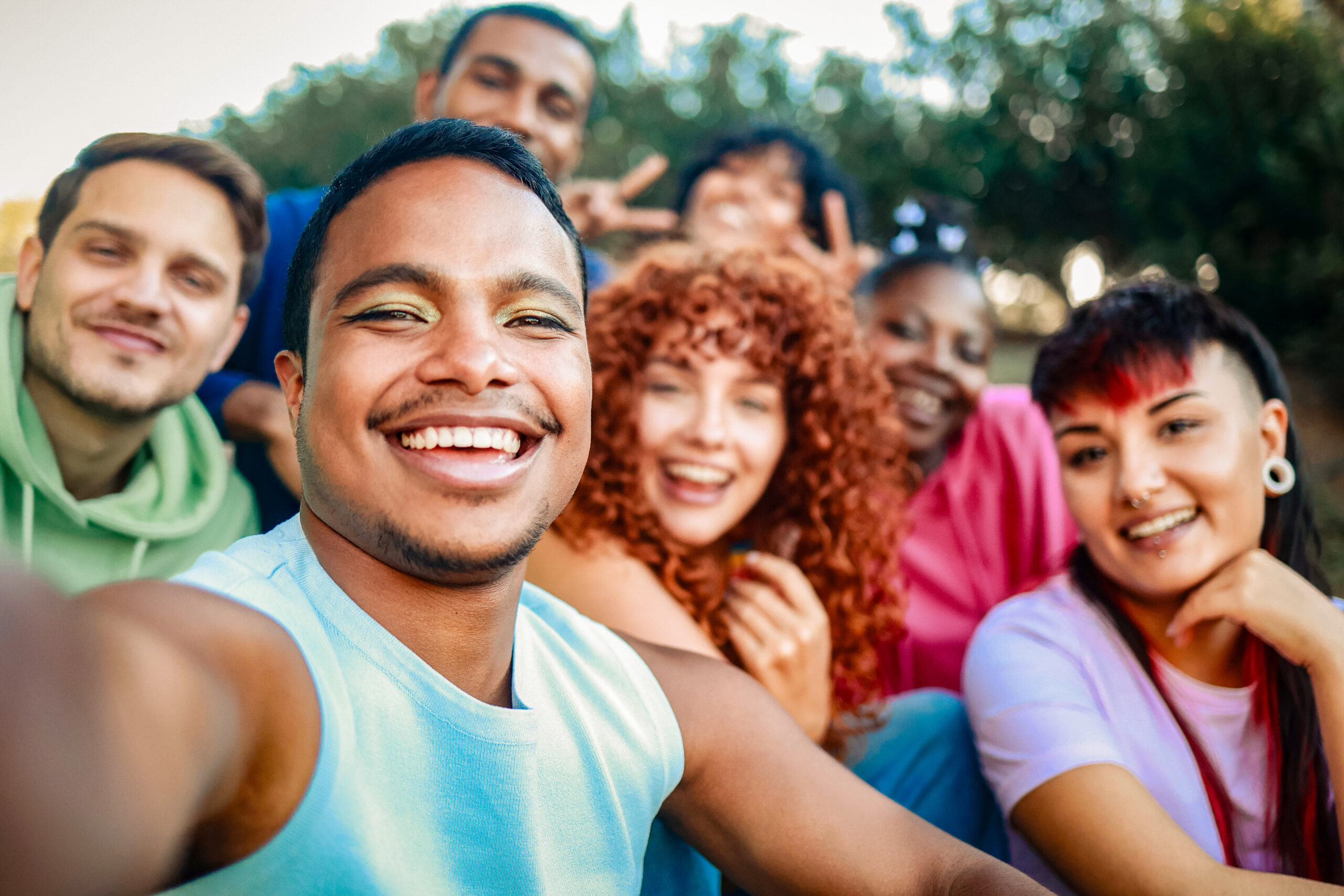 Young diverse people smiling at mobile phone camera at city park. African nonbinary taking selfie with friends. LGBT community
