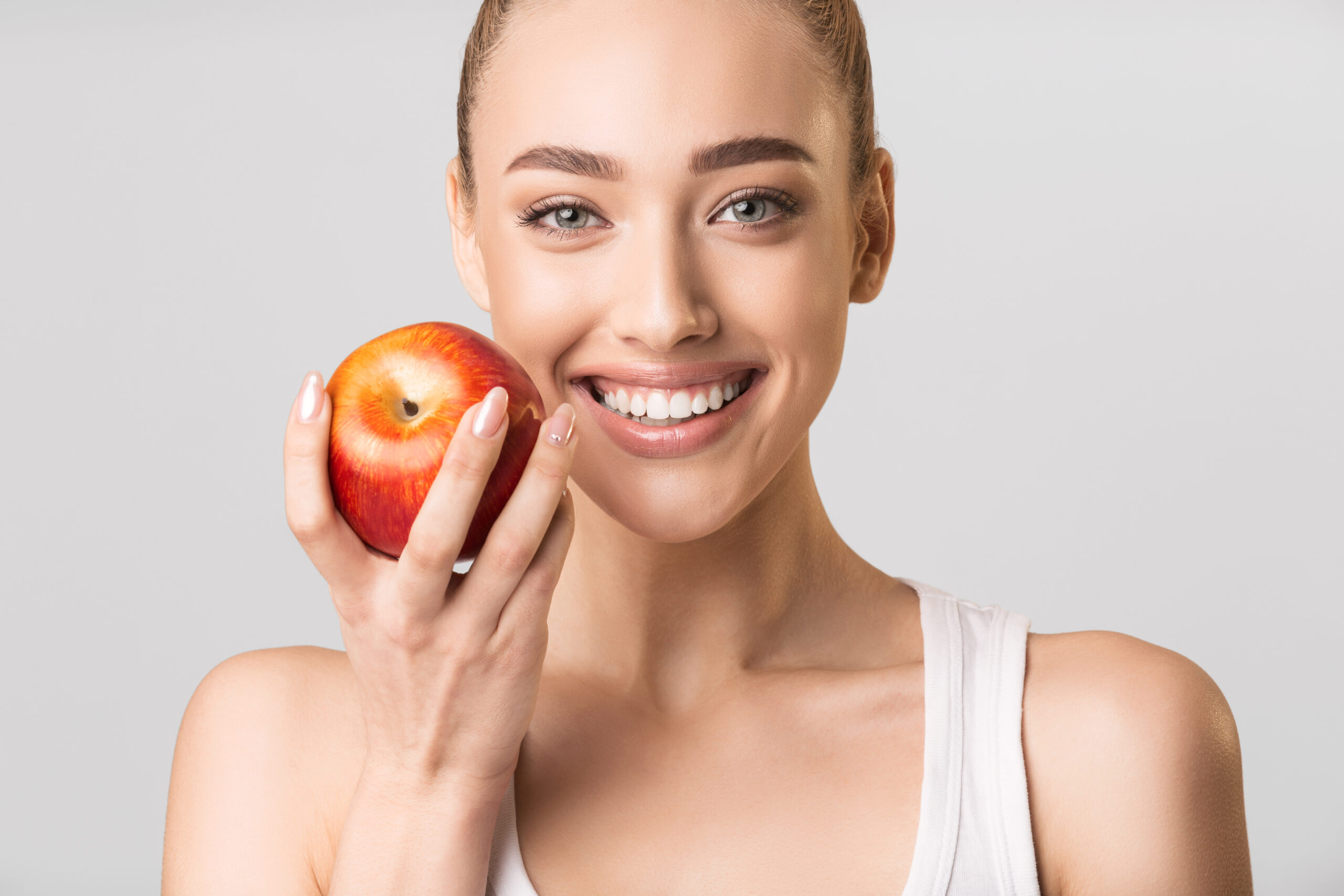 Woman With Perfect Smile Holding Apple Posing On Gray Background